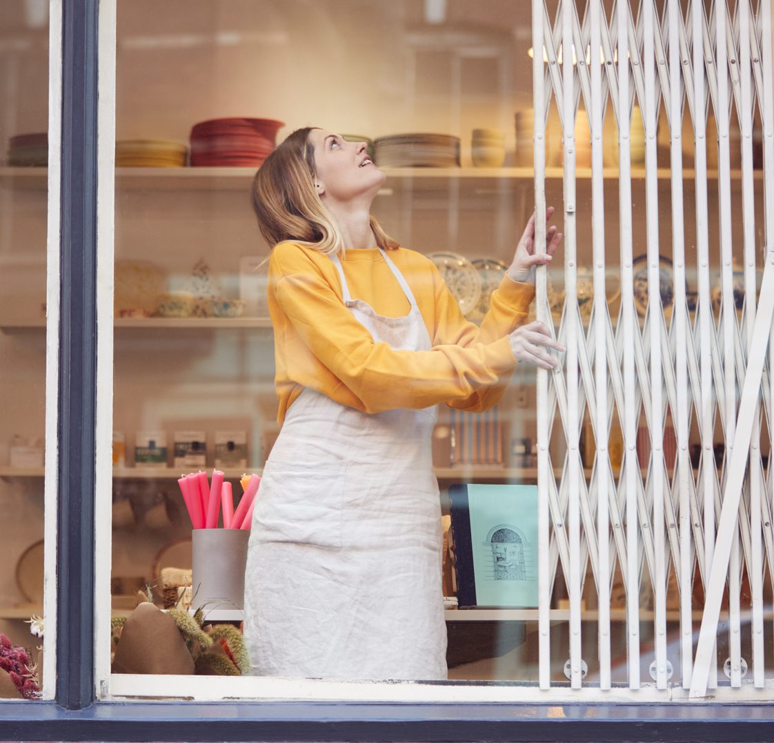 Mujer abriendo el cierre metálico de un negocio.