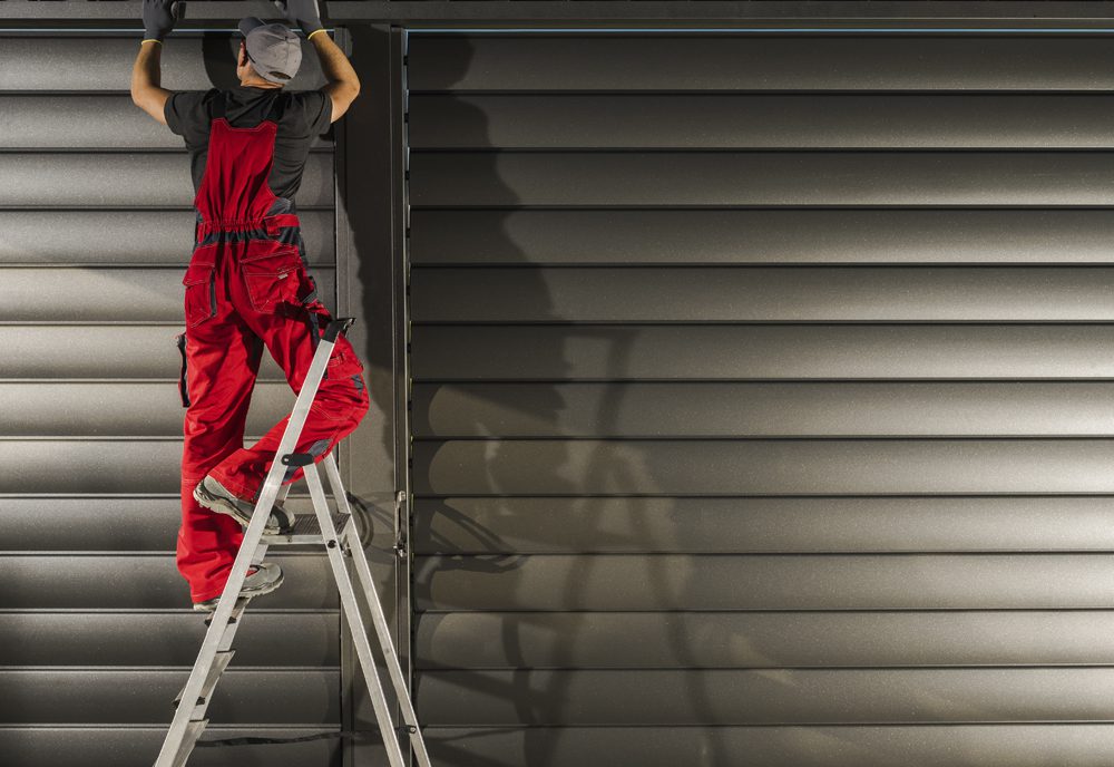 Servicio para automatismos Un cerrajero repara un cierre motorizado de una tienda o comercio.