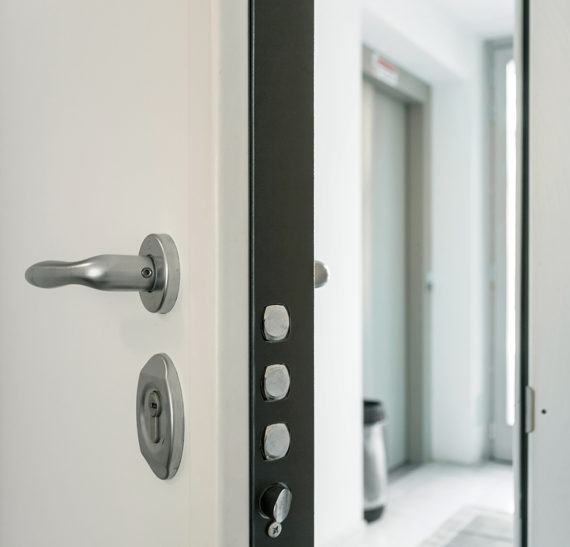 Puerta blindada de piso con cerradura multipunto y sistema de seguridad reforzado, abierta hacia el rellano de una comunidad de vecinos.