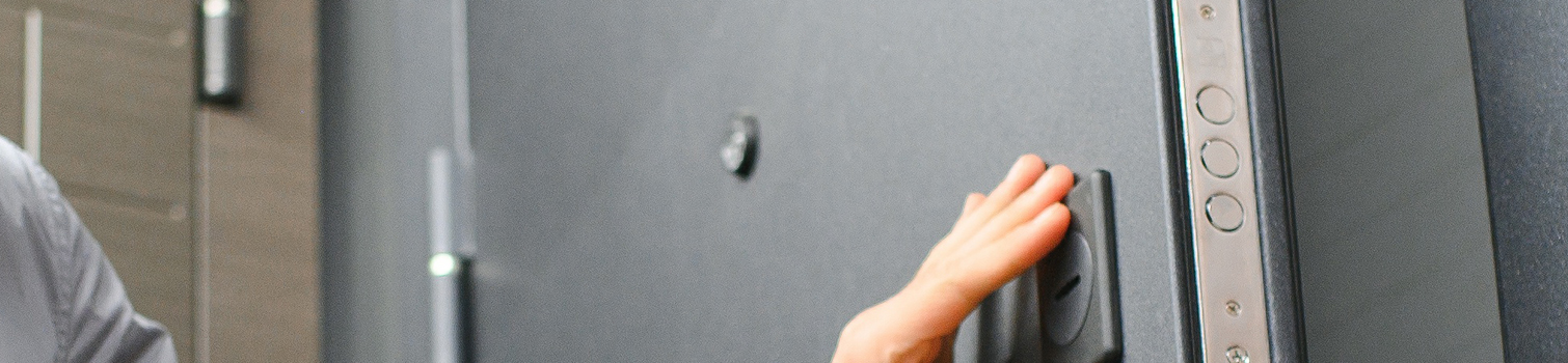 insights cinco mejoras piso interior uno Mano cerrando una puerta de seguridad de vivienda con mirilla, cerradura multipunto y refuerzos metálicos visibles en el marco.