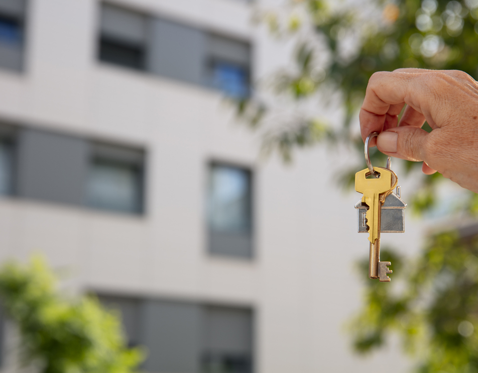 insights control entrega llaves Mano sosteniendo un juego de llaves frente a un edificio residencial, representando la gestión segura y el control de llaves maestras en comunidades de propietarios.