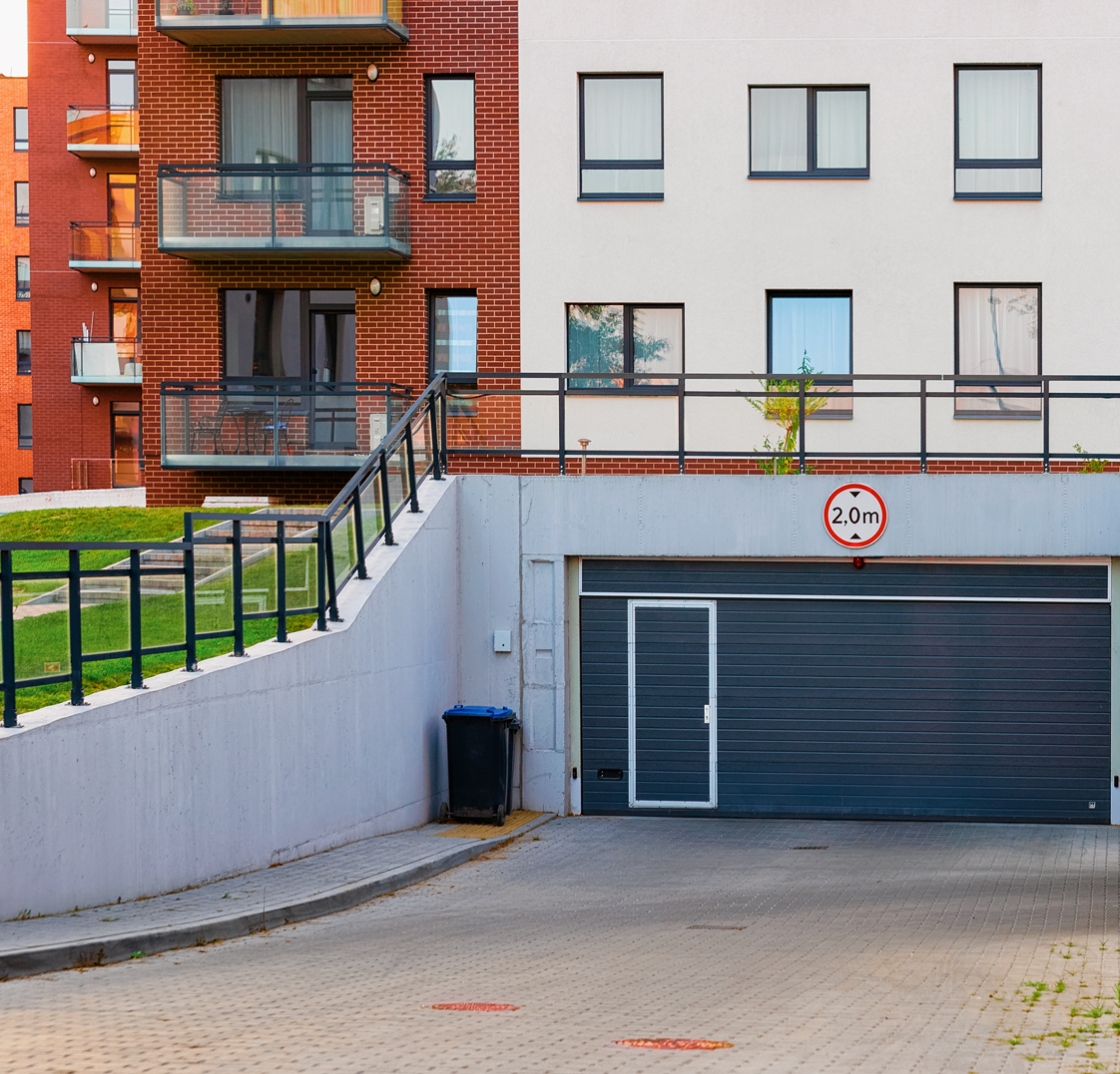 Entrada de garaje comunitario con puerta seccional y señal de gálibo, un área vulnerable que requiere cerraduras y sistemas de acceso seguros según keys cerrajeros.